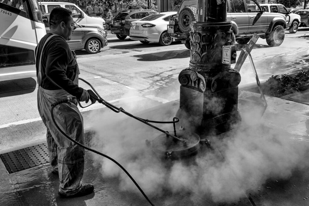 Black and white image of a man cleaning a street fixture in Seattle, showcasing urban work life.